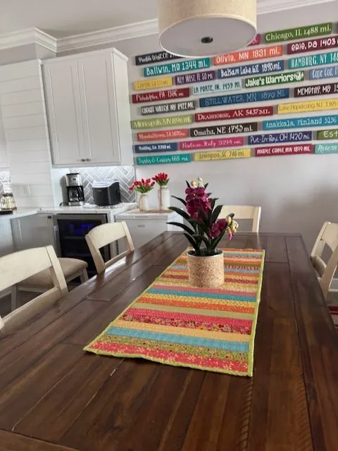 Dining area with a wall of colorful hometown mile-marker signs and a bright table runner.