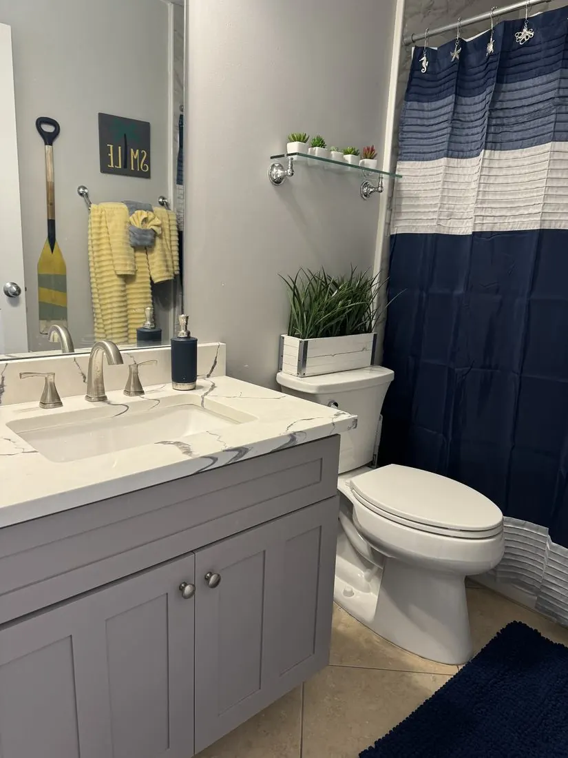 Guest bathroom with a navy and white striped shower curtain, marble vanity, and coastal accents.