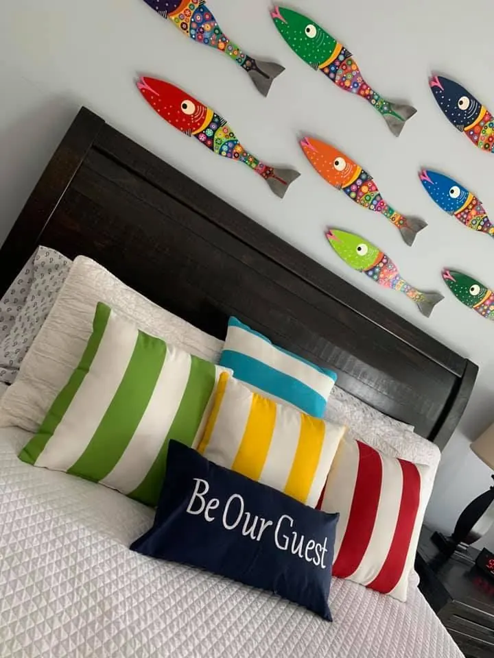 Guest bedroom with a school of colorful painted fish above the bed and a Be Our Guest pillow.