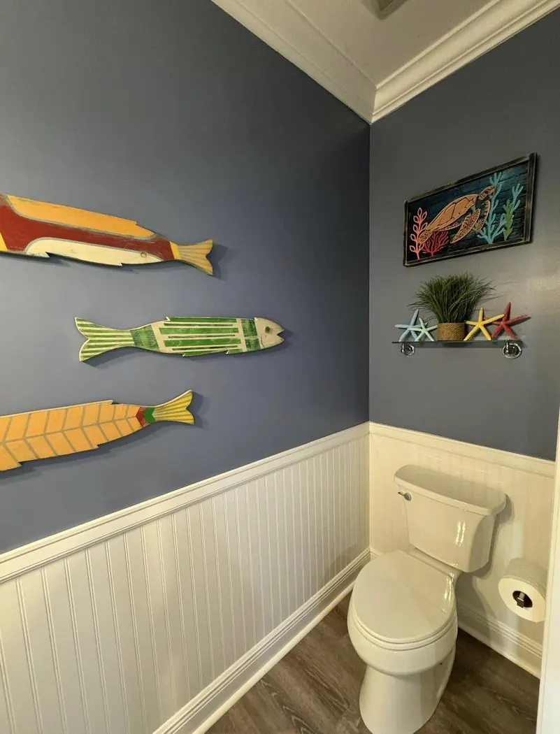 Powder room with navy walls, white beadboard wainscoting, and three carved wooden fish.