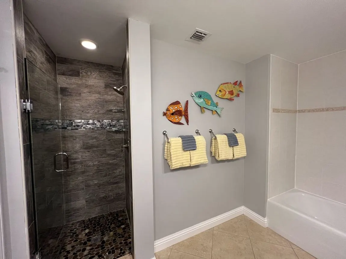Master bathroom with a glass shower, pebble floor, painted fish wall art, and yellow towels.